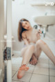 A woman sitting on the floor in a bathroom next to a sink.