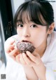 A woman eating a chocolate cookie in front of a window.