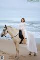 A woman in a white dress riding a horse on the beach.