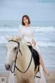 A woman in a white dress riding a white horse on the beach.