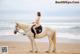 A woman riding on the back of a white horse on a beach.