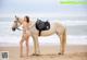 A woman in a bikini standing next to a horse on the beach.