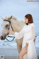 A woman in a white dress standing next to a white horse.