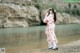 A woman in a pink kimono standing by a river.