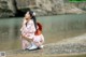 A woman in a pink kimono sitting on the shore of a river.