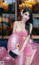 a woman in a pink dress sitting on an inflatable flamingo