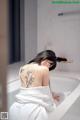 A woman sitting in a bathtub with a tattoo on her back.