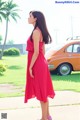 A woman in a red dress standing in front of a car.