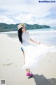 A woman in a white dress and hat on a beach.