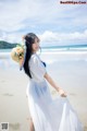 A woman in a white dress and hat on the beach.