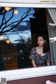 A woman standing in front of a window looking out at the night.