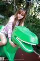 A woman sitting on top of a green dinosaur statue.