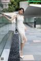 A woman in a white dress leaning against a glass wall.