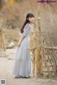 A woman in a blue dress standing next to a wooden fence.