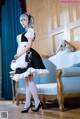 A woman in a maid outfit standing in front of a couch.