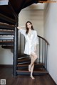 A woman in a white robe standing on a wooden staircase.