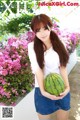 A woman holding a watermelon in front of flowers.