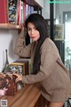 A woman leaning against a bookshelf in front of a bookcase.