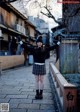 A woman in a black sweater and plaid skirt standing on a bridge.