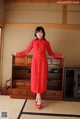 A woman in a red dress standing in front of a dresser.