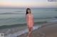 A woman in a pink dress standing on the beach.