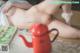 A naked woman laying on a bed next to a red teapot.