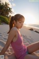 A woman in a pink tank top sitting on a beach.