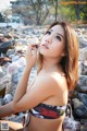 A woman in a bikini sitting on a rocky beach.