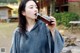 A woman in a gray hoodie drinking from a brown bottle.