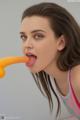 A young woman is licking an orange with her tongue.