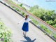 A woman in a white shirt and blue skirt walking down a road.