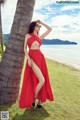 A woman in a red dress leaning against a palm tree.