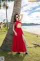 A woman in a red dress leaning against a palm tree.