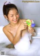 A young woman taking a bath with a toy gun.