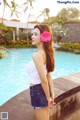 A woman with a flower in her hair standing by a pool.