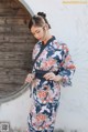 A woman wearing a blue and orange kimono standing in front of a wall.