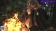 A woman sitting in front of a bonfire in the woods.