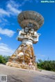 A woman standing in front of a large satellite dish.