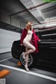 A naked woman standing next to a black car in a parking garage.