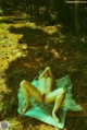 A naked woman laying on a blanket in the woods.