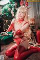 A woman in a red outfit sitting on the floor next to a Christmas tree.