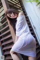 A woman in a white dress leaning against a wooden staircase.