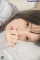 A young woman laying in bed with her hand on her chin.