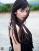 A woman with long black hair standing on a beach.