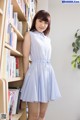 A woman in a blue and white dress standing in front of a bookshelf.