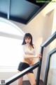 A woman in a white top and black skirt posing on a staircase.