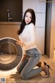 A woman kneeling on the floor next to a washing machine.