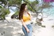 A woman in a yellow top and jeans standing on a beach.