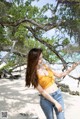 A woman in a yellow top and jeans standing on a beach.