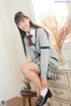 A young woman in a school uniform sitting on a dresser.